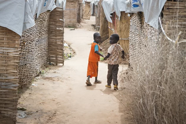 Two young refugee children from South Sudan walk back to their shelter at Al-Nimir camp in Sudan, the day before the High Commissioner's visit in mid-August 2017. ; Since December 2013, over 400,000 South Sudanese have fled to safety in neighbouring Sudan. Al-Nimir camp opened in April 2017 and by mid-August was hosting some 5,800 refugees, nearly all of them women and children from Western Bahr el Ghazal State. As worsening violence continues to force people from their homes in South Sudan, the UN High Commissioner for Refugees Filippo Grandi, visited refugees and the host community in Al-Nimir and called on warring parties, regional states and the international community to urgently establish peace. Conflict and drought have displaced nearly four million South Sudanese both inside the country and beyond its borders. Efforts to restore peace have so far proven unsuccessful.
