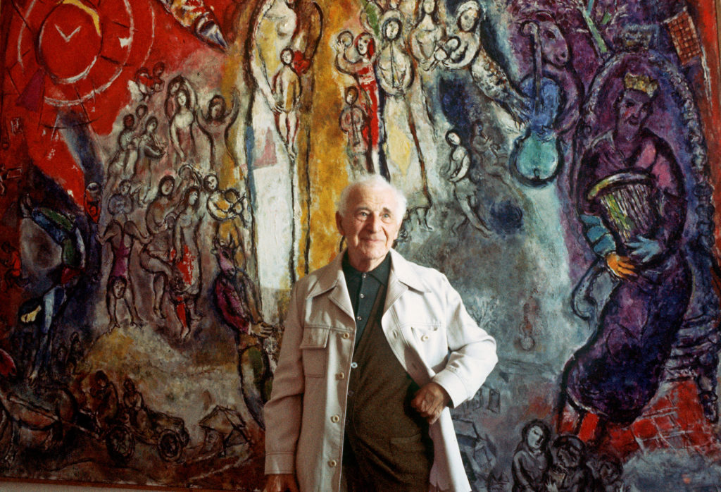 famous painter Marc Chagall, born in Vitebsk, Belarus, poses 02 July 1977 in front of one of his works, inspired with 25 others by Old and New Testament and gathered in Nice for an exhibition in honour of his 90th anniversary. He began to design ballet sets and costumes, illustrated several books, but is best known for his fanciful painting of animals, objects and people of his life, dreams and Russian folklore. / AFP PHOTO / STAFF