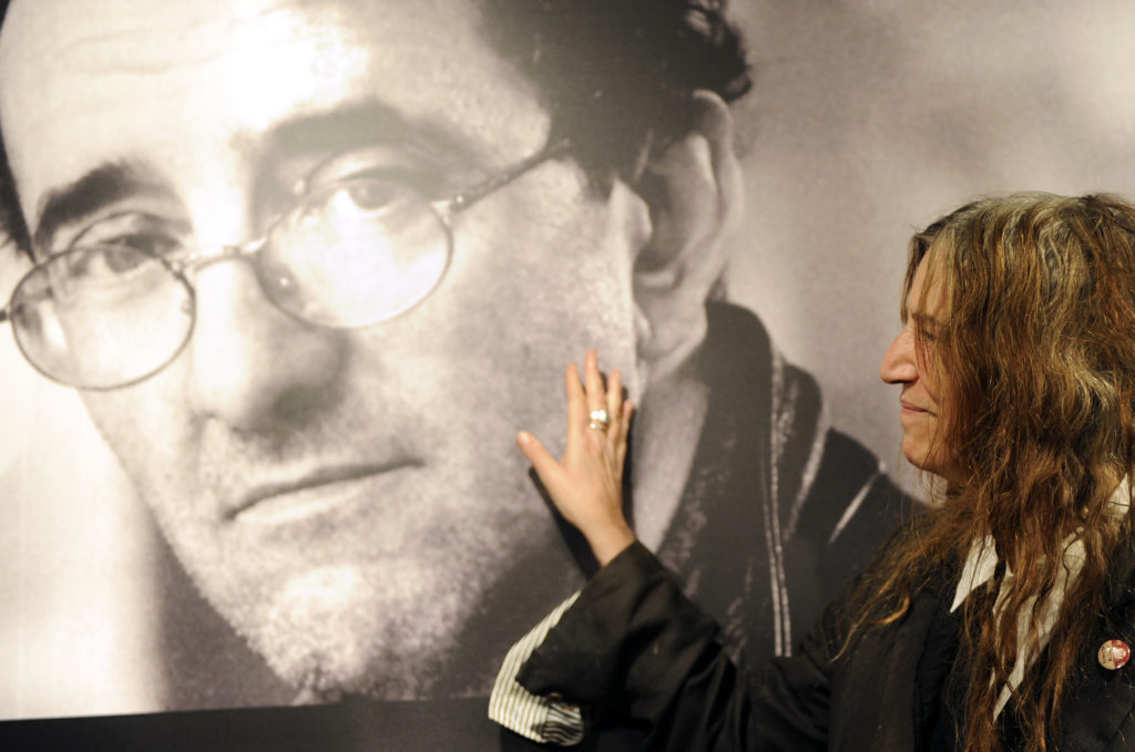 US singer Patti Smith poses in front of a giant poster of late Chilean writer Roberto Bolano in Madrid on November 26, 2010 during a ceremony at the Casa de America, announcing a week paying tribute to Bolano.   AFP PHOTO/ DOMINIQUE FAGET (Photo by DOMINIQUE FAGET / AFP)