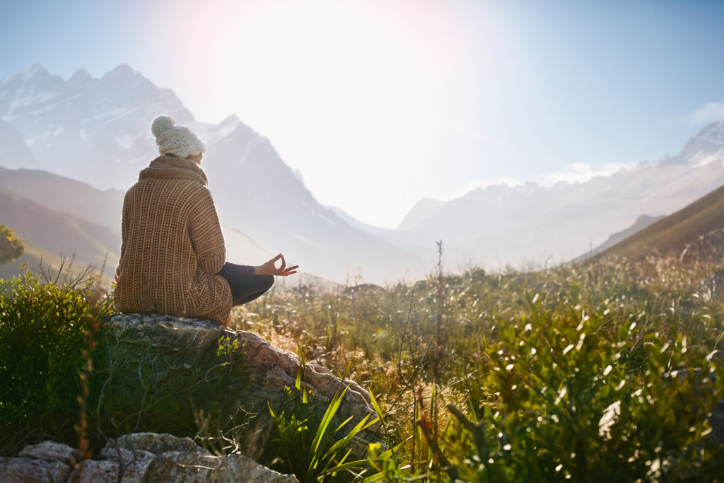 Young woman meditating on rock in sunny, remote valley.