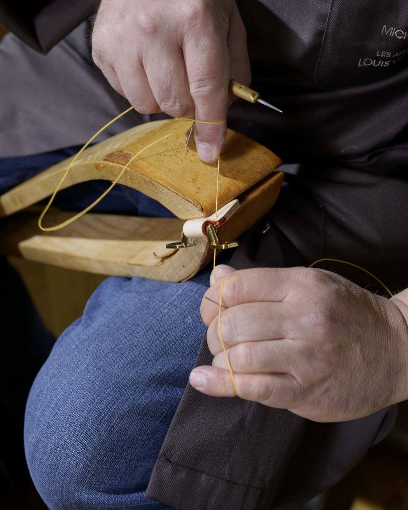 這是Asnières工場保存下來的傳統馬鞍縫紉法，圖中工匠正以兩支針穿上蜜蠟麻線鞏固行李箱上的牛皮手柄。
