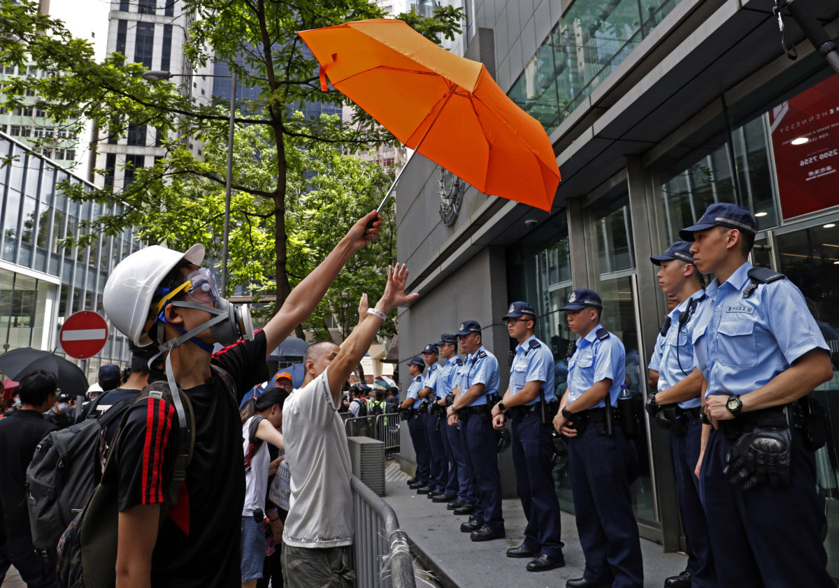 6月21日，示威者包圍警察總部，要求警方撤回對6.12事件的暴動定性。余偉建以警方與示威者對峙及示威者舉起雨傘的畫面，交代事件。（AP Photo/Vincent Yu）