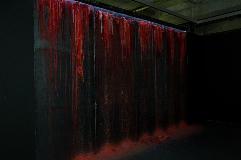 作品《意志的幽靈》的紅蠟沿牆身流到地面，形成一條條蠟痕。