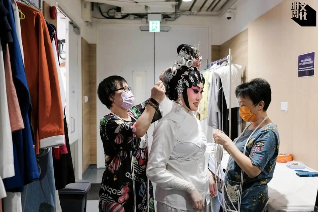 在行內稱「衣箱」的戲服助理，正在為準備上台演出的陳禧瑜穿上戲服。