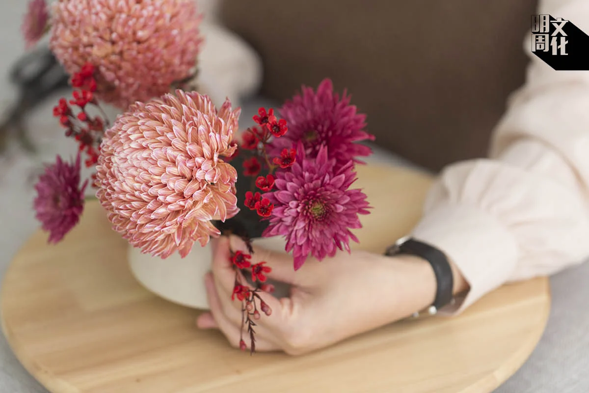 放上蠟梅,在左右兩邊插上石斛蘭,並加入金松,突出劍蘭和牡丹菊。Cherie指,此作的鮮花四散,能營造出自然的感覺。若左右兩邊花材的闊度加起來等同花盆的闊度,便是黃金比例。