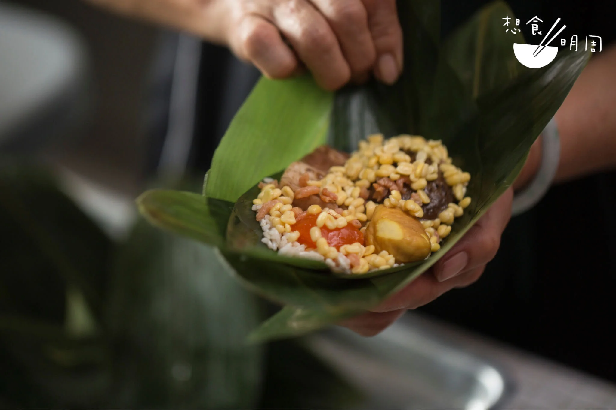 工場内，Joephy找到相熟「阿姨」幫手包糉。事先用醬油煮過的花菇、以味 醃煮的豚腩，連同北海道瑤柱、鹹蛋黄等等，逐一放入，合組成傳統糭滋味。