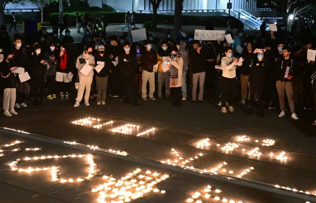在加州大學裏的集會，出席人士高舉白紙和標語，在燭光前站立。