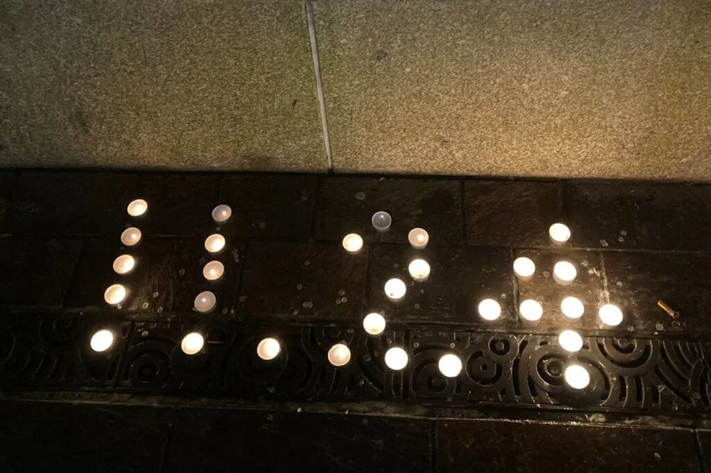 L在英國參與校園裏的悼念會，蠟燭排列出「11.24」字樣，正是烏魯木齊大火發生的日子。