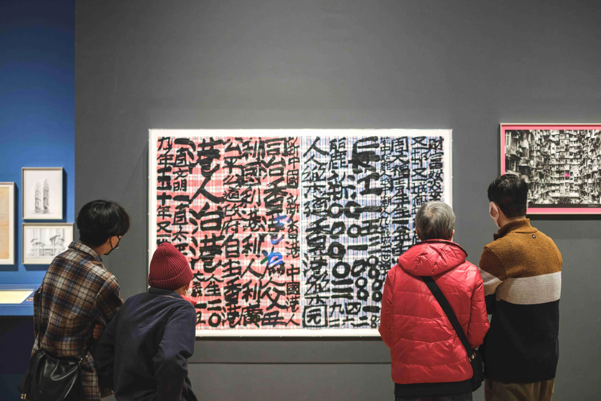 四人正於「香港：此地彼方」展廳內，觀看「九龍皇帝」曾灶財的書法作品。