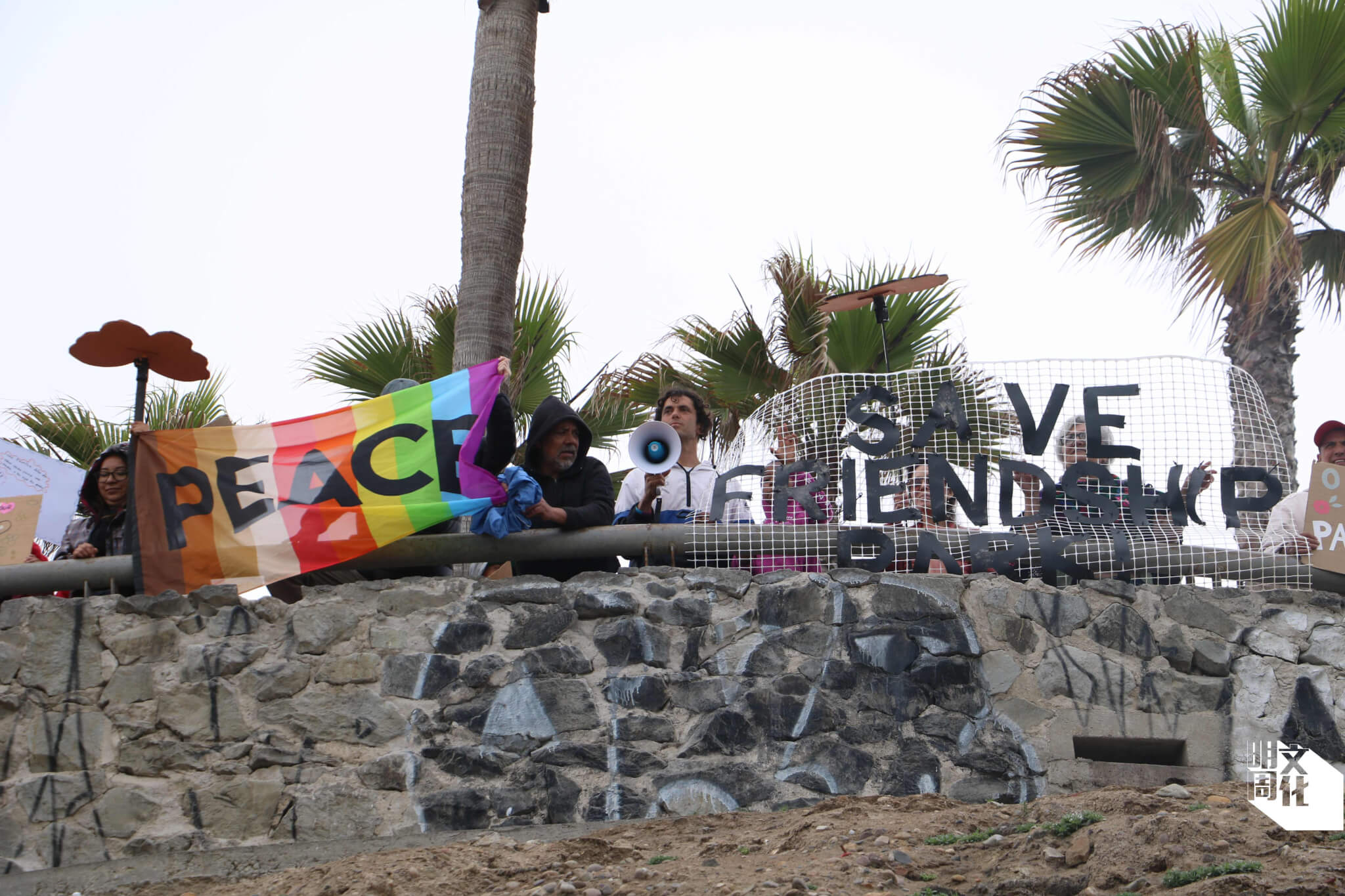 參與者手持印上「Peace」的彩虹旗、「Save Friendship Park」等標語，走到觀景台向聖地牙哥的參與者揮手。