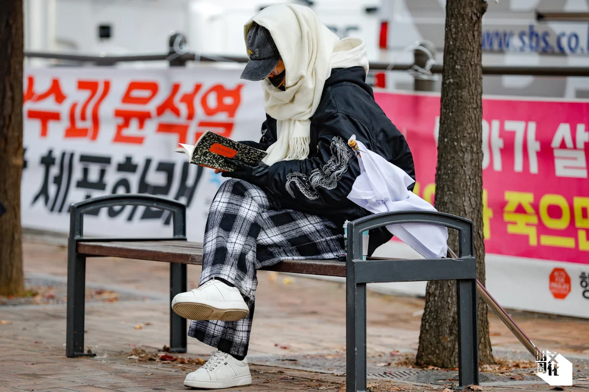 二○二四年十二月十一日,在首爾汝矣島呼籲彈劾總統尹錫悅集會中,一名參與者閱讀韓江著作《少年來了》。小說中,男孩之死引發了對光州事件的探索。