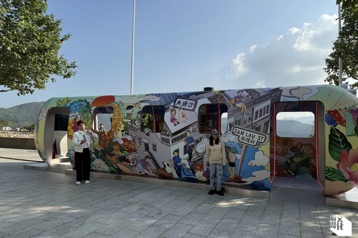 《沙角號列車》 創作者：何博欣 地點：沙頭角海濱休憩處 作品介紹：滿載創意與沙頭角居民日常生活景象的《沙角號列車》，以火車車廂作為畫布，由香港藝術家何博欣透過充滿活力和色彩的插畫，將沙頭角獨特的歷史文化與居民日常生活呈現當中。 透過這卡列車上的插畫，遊人可以觀賞沙頭角商店、街頭小販和街坊之間過往日常的互動，不單突顯該區不斷變化的風貌，亦連結昔日的社區情懷。藝術家突破傳統美學觀念，創作風格看似真實卻又怪誕，為陸上龍舟與魚燈舞等沙頭角特色節慶場景入了幽默與超現實主義，彷如置身夢境。匯聚於列車中各式的多媒體沉浸式體驗，加強了敘事效果，讓遊客體驗區內精彩的傳統文化，感受居民日常生活情境。隨著沙頭角進一步開放，《沙角號列車》不單向該區歷史及文化致敬，亦以創新方法邀請大家探索編織於沙頭角中的豐盛故事。