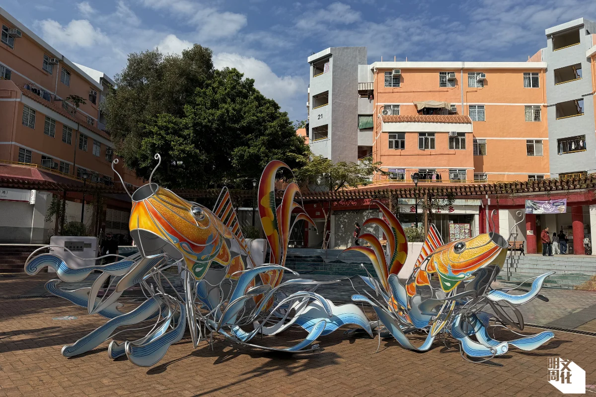 《魚躍共舞》 創作者：杜煥 地點：沙頭角廣場 作品介紹：香港藝術家杜煥於紮作工藝家庭中成長，耳濡目染之下，啟蒙他對各種手藝的興趣。搬進長洲居住後，當地的紥作工藝品撩動起他的童年往事，重新激發他對這項傳統的熱誠與創造力。藝術家把沙頭角的魚、海邊及象徵禁區的鐵絲網等幾個元素融合在他的作品中，緊扣著他的藝術旅途，促成深富沙頭角文化和生活特色的《魚躍共舞》。 他將沙頭角廣場轉化成舞台，活現大海的靈動神髓，以傳統的紮作技巧加上現代金屬藝術的設計，創造沉浸式的藝術場景，讓「魚兒」躍起浪花。藝術家於現場為作品塗上顏色，為沙頭角加添活力色彩，同時以《魚躍共舞》展現大自然與人之間的和諧，並描繪中國人對豐衣足食的「有餘」感覺，體現漁民與海的相依關係。