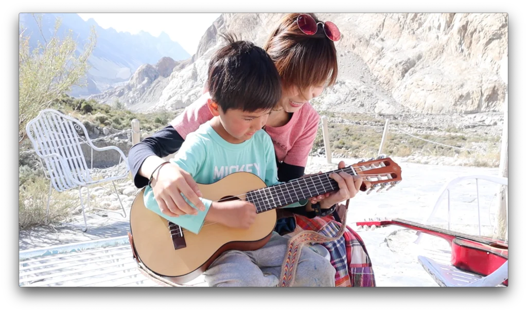 慧敏抱着路過的小孩一起合奏一曲，她負責按弦，小孩負責彈奏。