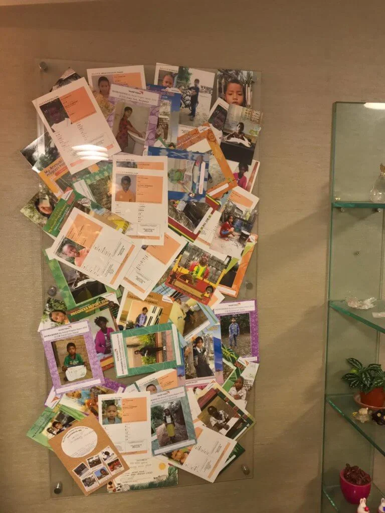 艾威多年來助養了近三十名貧困兒童，他將這些助養子女寄來的相片及畫都掛在客廳一角。